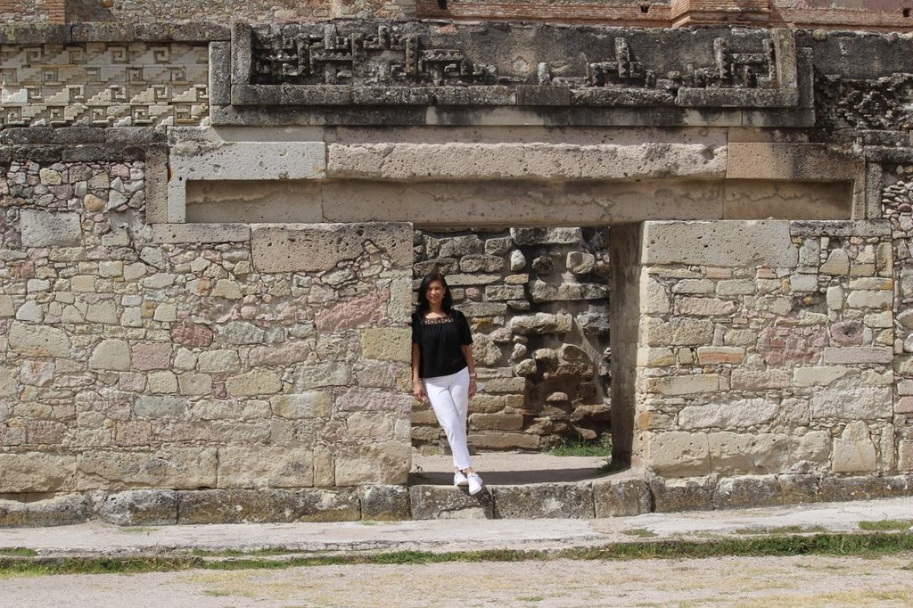 Woman standing in front of the ancient stone mosaic walls of the Mitla ruins.