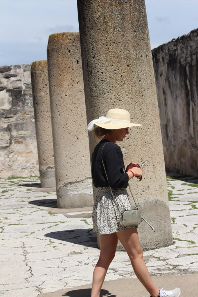 A visitor exploring the sunny ancient stone columns of the Mitla ruins.